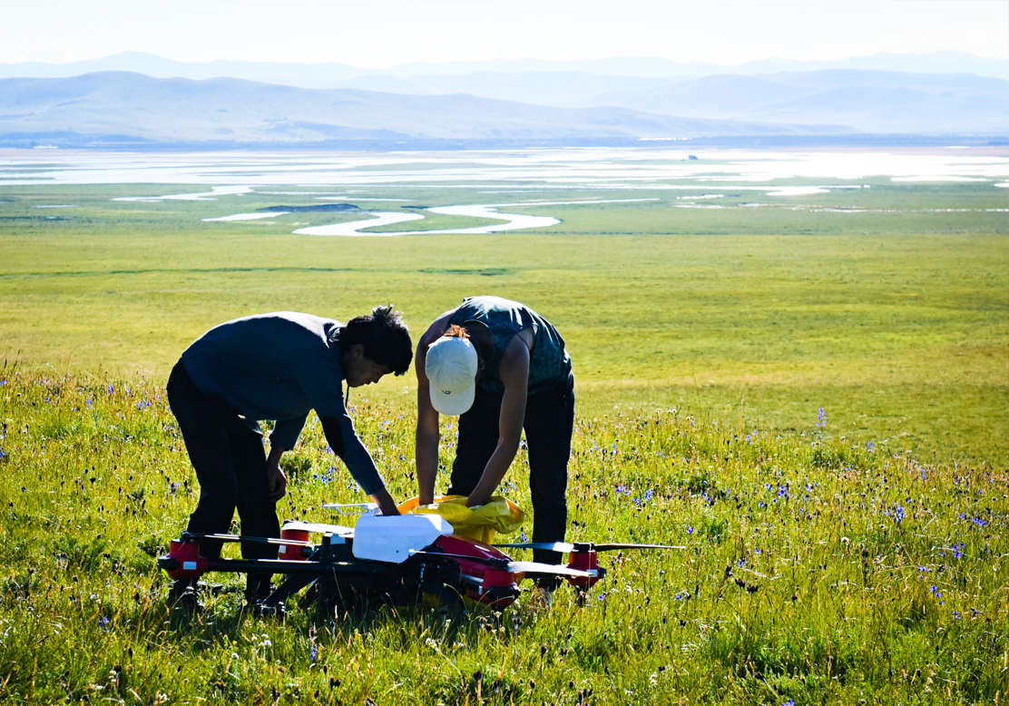 Two young herdsmen poured grass seeds into the tank of their newly bought drone, which they consider a new hope to protect their beloved pasture that was subject to degradation, Hongyuan, Sichuan, China. June 2021.